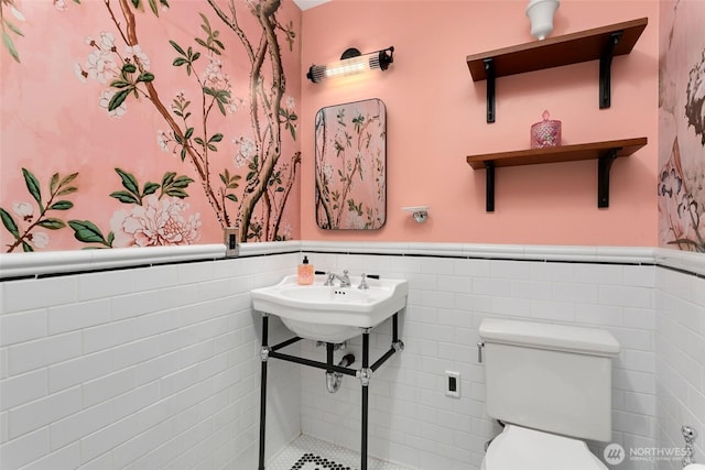 bathroom featuring tile walls, toilet, and a wainscoted wall