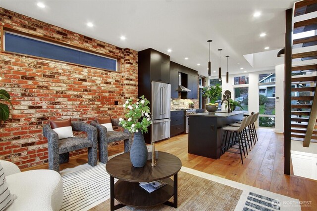 living area with stairway, recessed lighting, light wood-type flooring, and brick wall