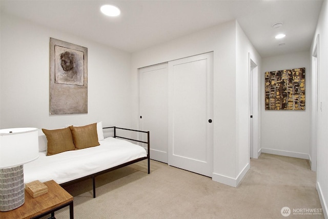 bedroom with a closet, recessed lighting, light colored carpet, and baseboards