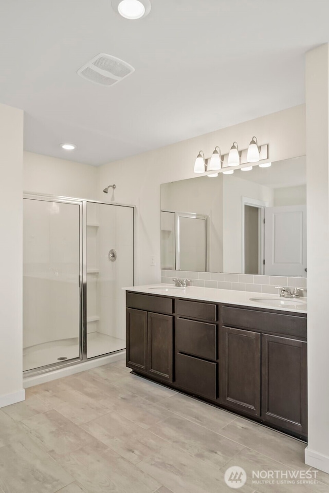 bathroom featuring a shower stall, double vanity, and a sink