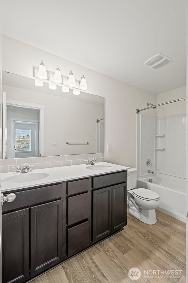 full bath with wood finished floors, visible vents, double vanity, a sink, and toilet