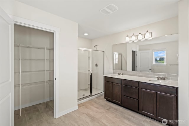 full bath with a walk in closet, double vanity, a stall shower, and a sink