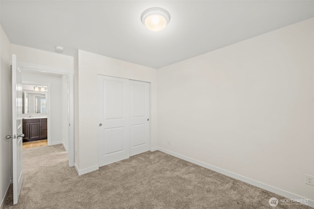 unfurnished bedroom with a closet, light colored carpet, and baseboards