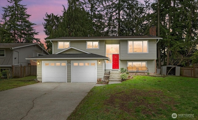 raised ranch with concrete driveway, fence, a lawn, and a chimney