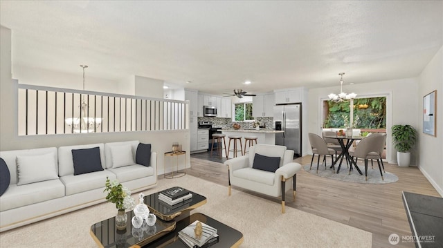 living room with baseboards, light wood-style floors, and ceiling fan with notable chandelier