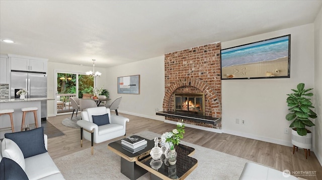 living area with light wood finished floors, a brick fireplace, baseboards, a chandelier, and recessed lighting