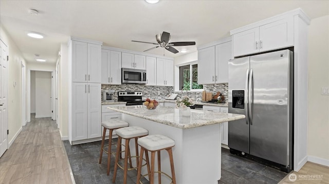 kitchen with a breakfast bar, stainless steel appliances, white cabinetry, backsplash, and a center island