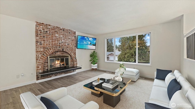 living room featuring a brick fireplace, wood finished floors, and baseboards