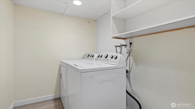 washroom featuring washing machine and clothes dryer, laundry area, baseboards, and wood finished floors