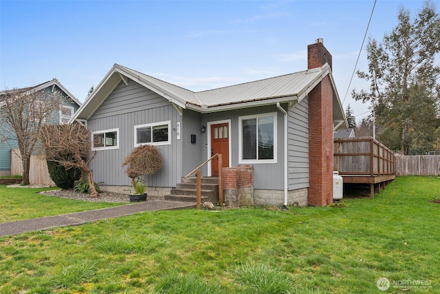 view of front facade with a front yard, metal roof, fence, and a chimney