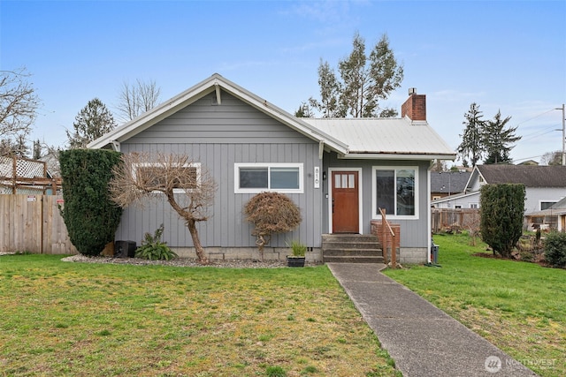 view of front of property featuring a front lawn, entry steps, fence, metal roof, and a chimney