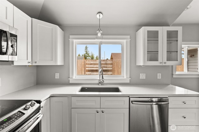 kitchen with glass insert cabinets, light countertops, stainless steel appliances, white cabinetry, and a sink