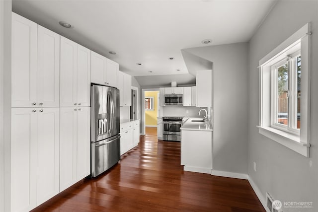 kitchen with a sink, dark wood-style floors, appliances with stainless steel finishes, white cabinets, and baseboards