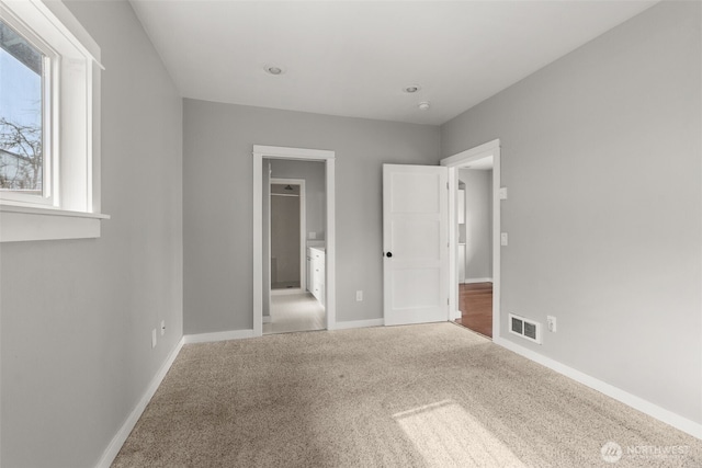 unfurnished bedroom featuring visible vents, carpet flooring, ensuite bathroom, and baseboards