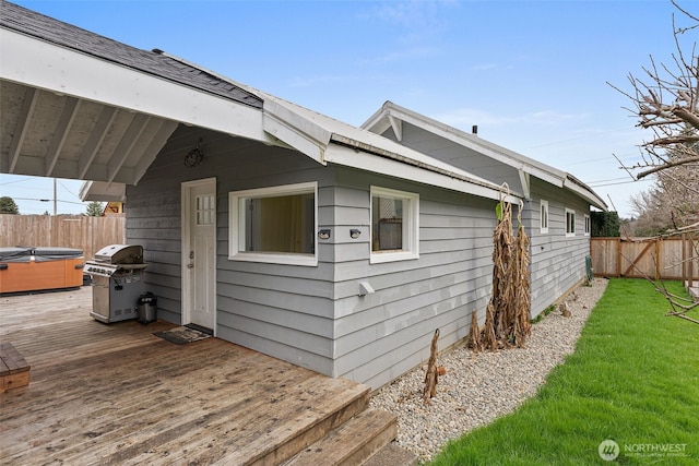 view of side of property with a deck, a yard, fence, and a hot tub