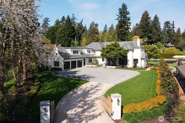 view of front of property featuring a front lawn, an attached garage, driveway, and a chimney