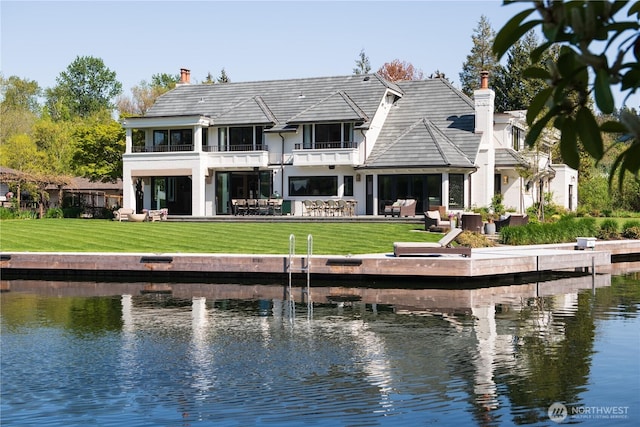 back of property featuring a balcony, a yard, a water view, and a chimney