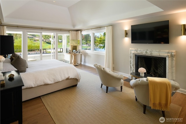 bedroom featuring a tray ceiling, a premium fireplace, wood finished floors, and access to exterior