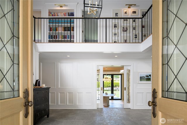 entryway with a notable chandelier, stone tile flooring, a towering ceiling, and a decorative wall