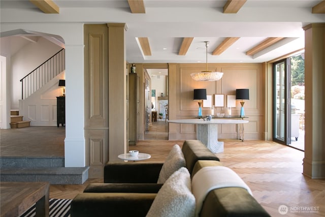 living room featuring stairs, beam ceiling, arched walkways, a decorative wall, and ornate columns