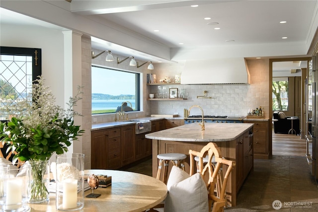 kitchen with custom range hood, plenty of natural light, a kitchen island with sink, and backsplash