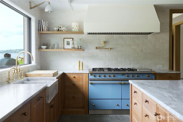 kitchen featuring backsplash, premium range hood, range with two ovens, light stone counters, and a sink