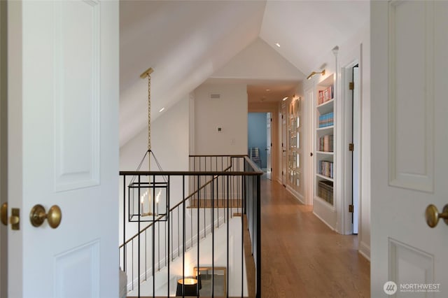 hallway with a chandelier, an upstairs landing, wood finished floors, and vaulted ceiling