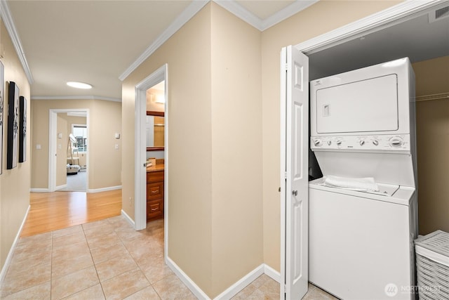 laundry area with ornamental molding, light tile patterned floors, stacked washer / drying machine, baseboards, and laundry area