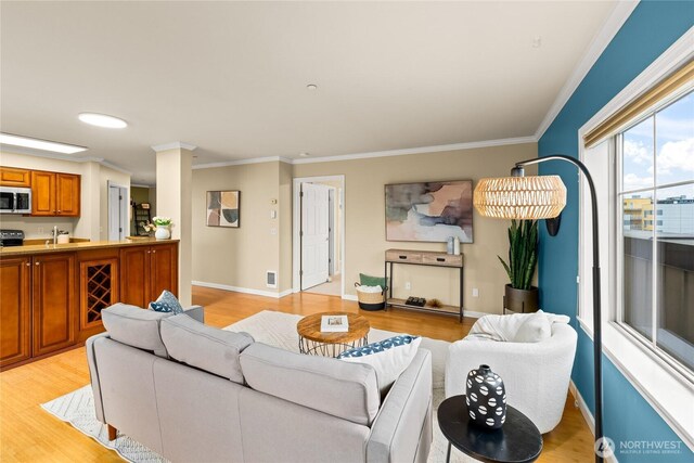 living area featuring visible vents, baseboards, light wood-style floors, and crown molding