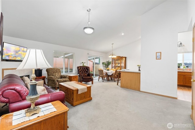 living area with a notable chandelier, high vaulted ceiling, plenty of natural light, and light carpet