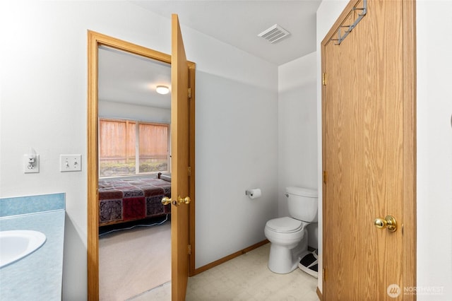 ensuite bathroom featuring tile patterned floors, visible vents, toilet, a sink, and baseboards