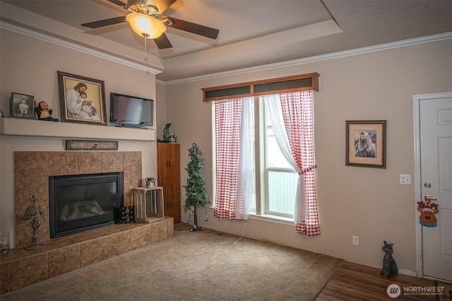 living area with a tray ceiling, crown molding, and a tile fireplace