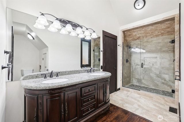 bathroom with double vanity, wood finished floors, a stall shower, and a sink