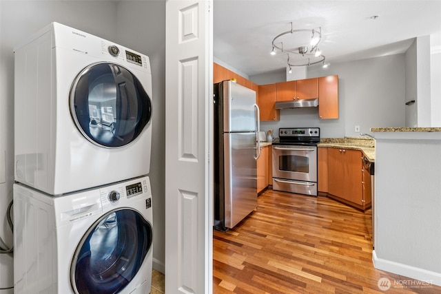 clothes washing area featuring rail lighting, light wood-type flooring, laundry area, and stacked washing maching and dryer