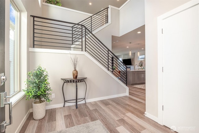 staircase featuring recessed lighting, a high ceiling, baseboards, and wood finished floors