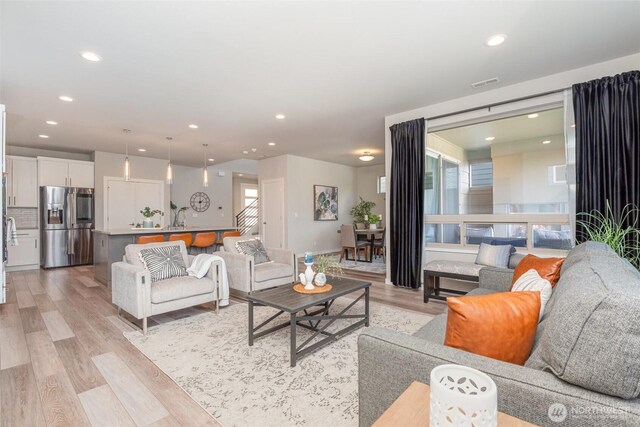 living area with recessed lighting, visible vents, light wood-style flooring, and stairway