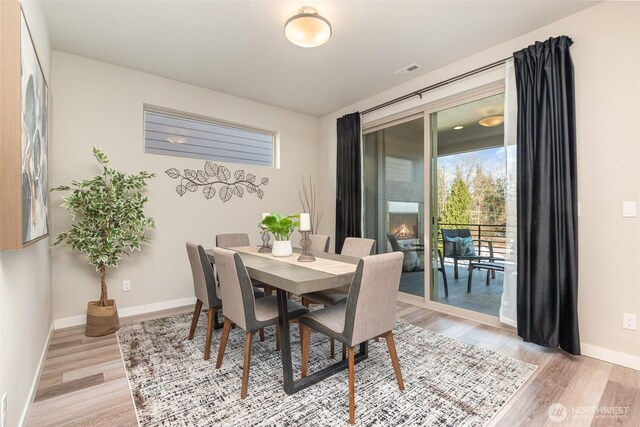 dining space featuring light wood finished floors, visible vents, a fireplace, and baseboards