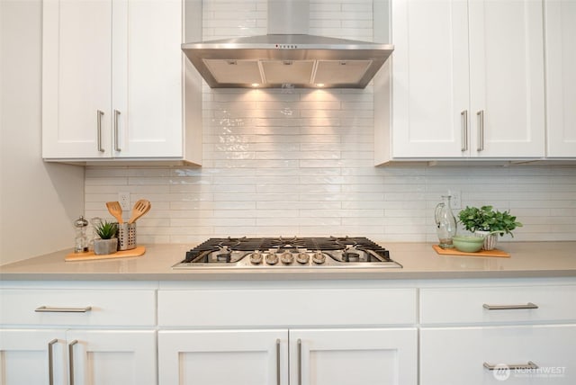 kitchen with wall chimney range hood, backsplash, white cabinets, light countertops, and stainless steel gas cooktop