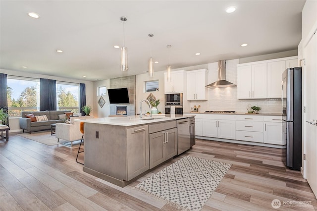 kitchen featuring wall chimney range hood, open floor plan, decorative backsplash, appliances with stainless steel finishes, and a sink