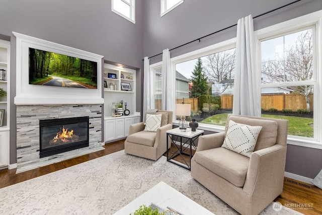 living area with a fireplace, wood finished floors, baseboards, and a towering ceiling