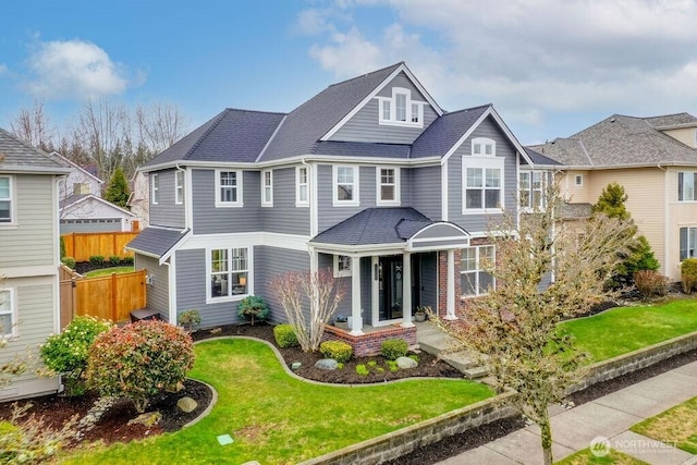 view of front of home featuring a shingled roof, a front lawn, and fence