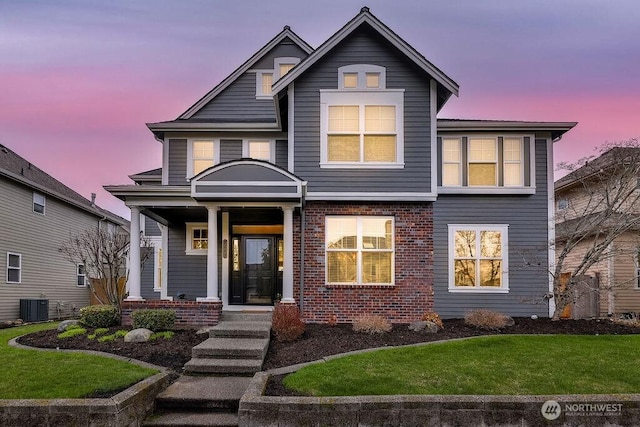 view of front of house with central air condition unit, brick siding, a porch, and a lawn