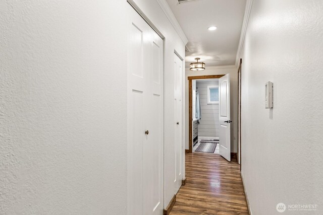 corridor with dark wood-style floors, baseboards, a textured wall, and ornamental molding