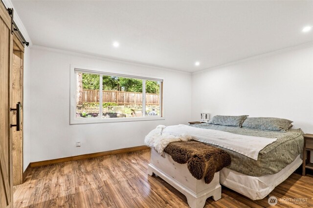 bedroom with a barn door, baseboards, wood finished floors, and ornamental molding