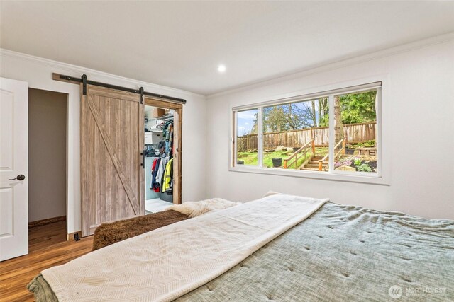 bedroom featuring wood finished floors, a walk in closet, a barn door, and ornamental molding