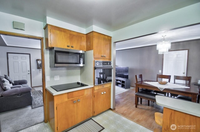 kitchen with a notable chandelier, black appliances, brown cabinetry, and light countertops