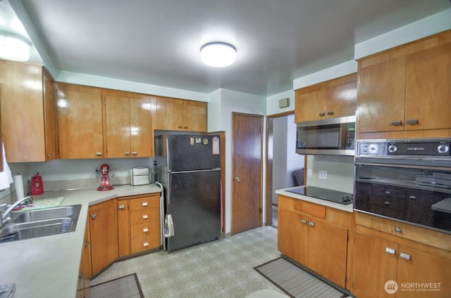 kitchen with brown cabinets, black appliances, light countertops, and a sink