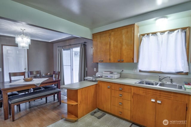 kitchen with brown cabinetry, a peninsula, light countertops, and a sink