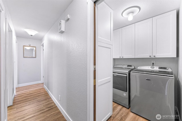 laundry area featuring baseboards, light wood-style floors, a textured wall, cabinet space, and separate washer and dryer