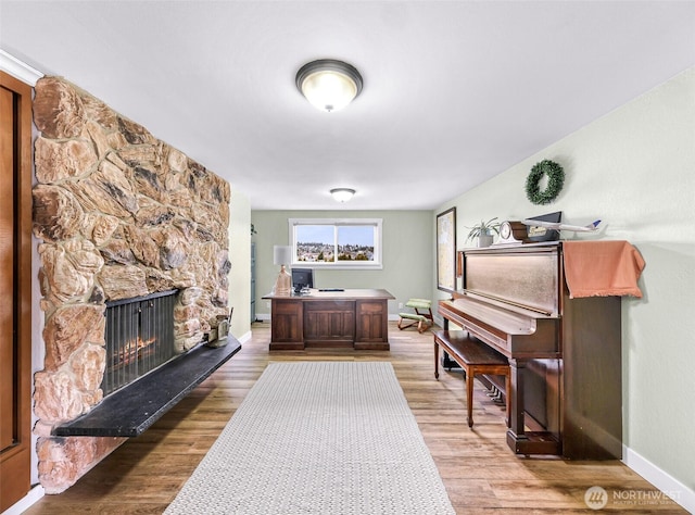 home office with light wood-type flooring, baseboards, and a stone fireplace